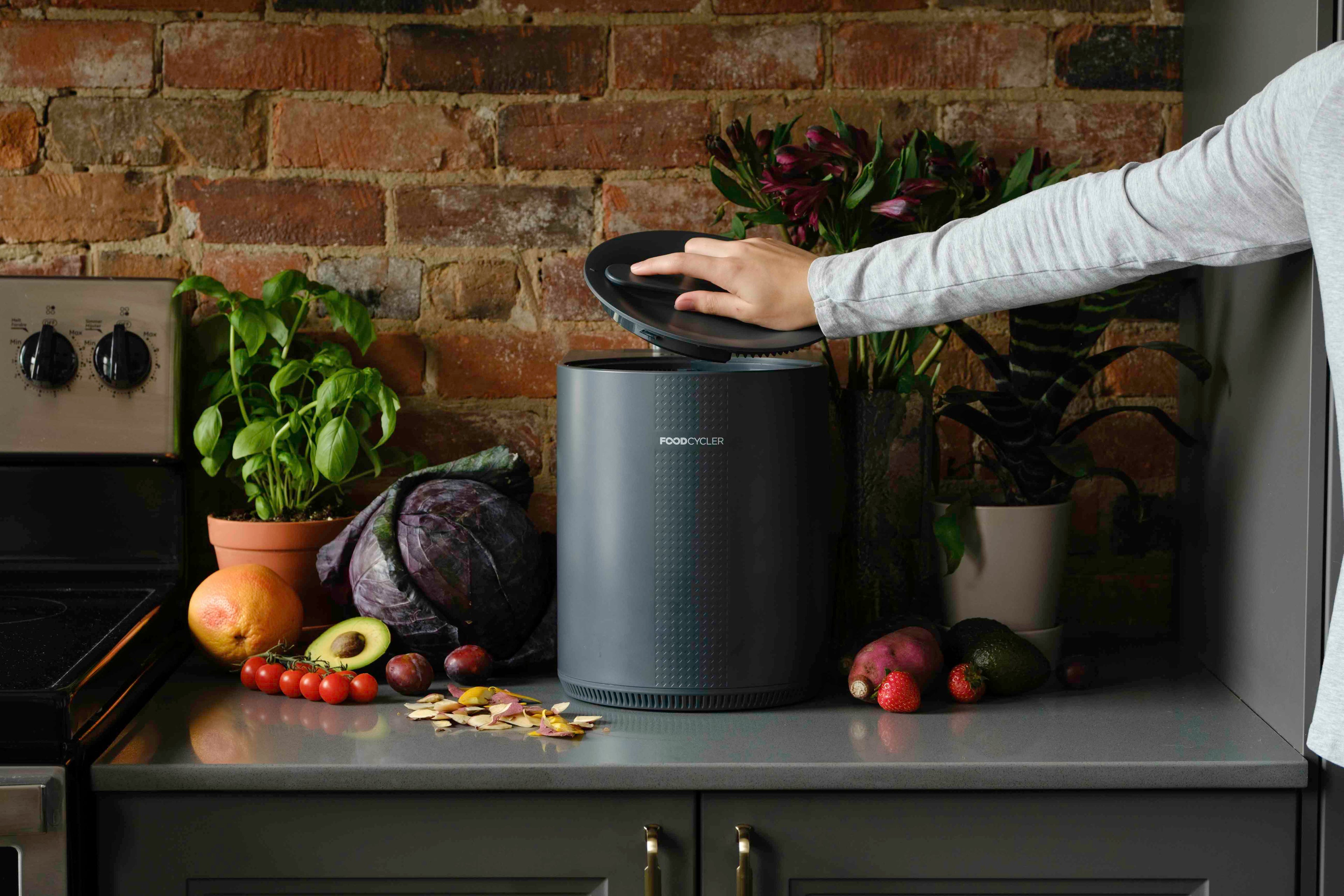 Grey FoodCycler Eco 3 on a kitchen counter with a person putting the lid on